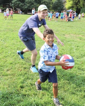DEAN Explorers camper running with a ball as a counselor chases during Sports & Games Camp