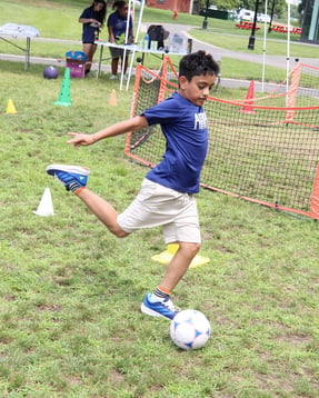 DEAN Achievers camper kicking a soccer ball at Sports & Games Camp