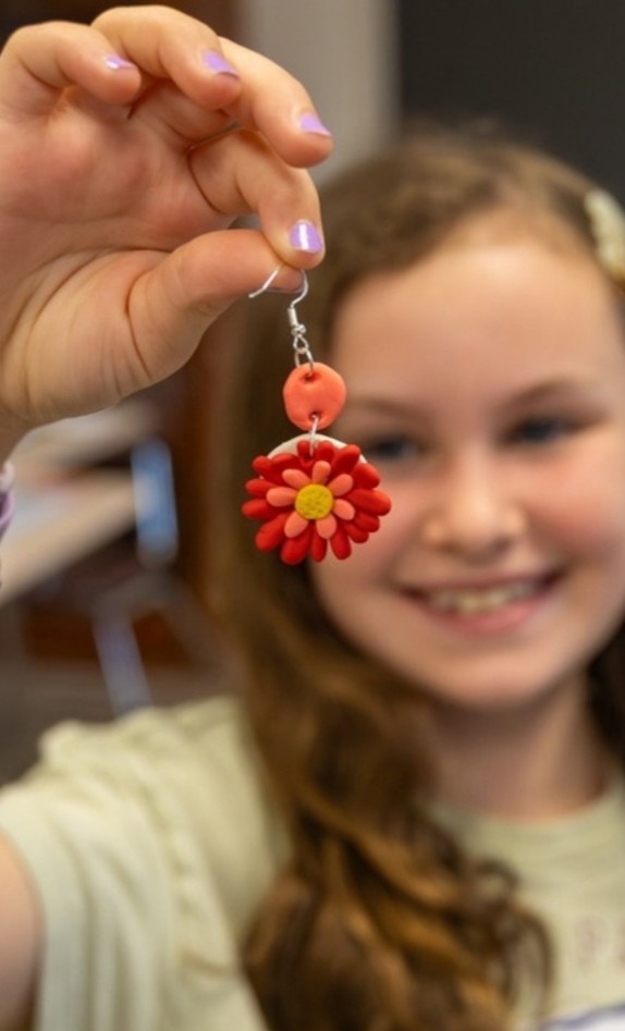 Camper holding up a flower earring she made in Design & Style camp