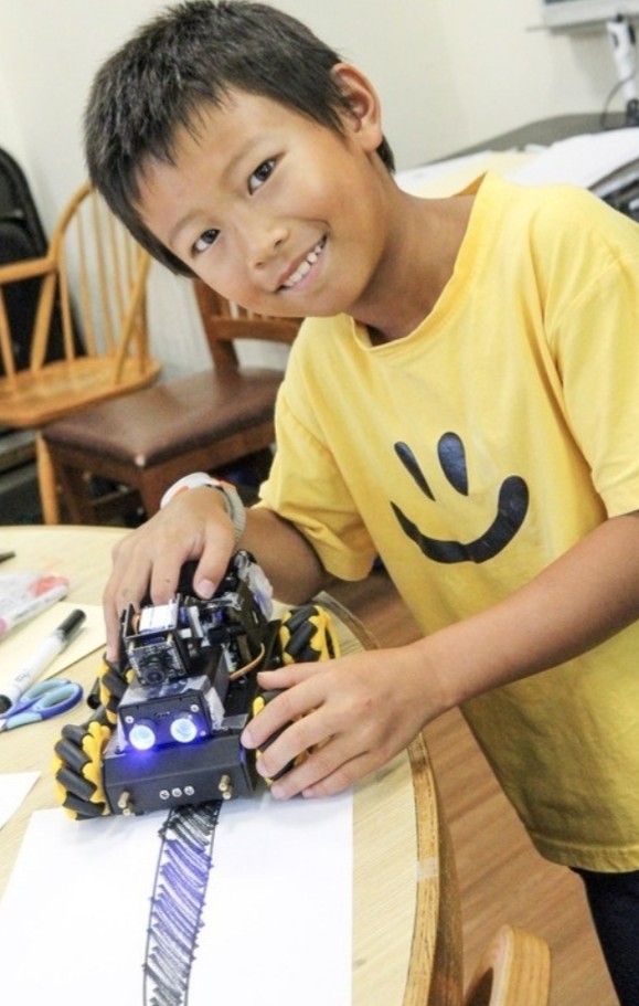 Camper smiling with a line-tracking robot in STEAM camp